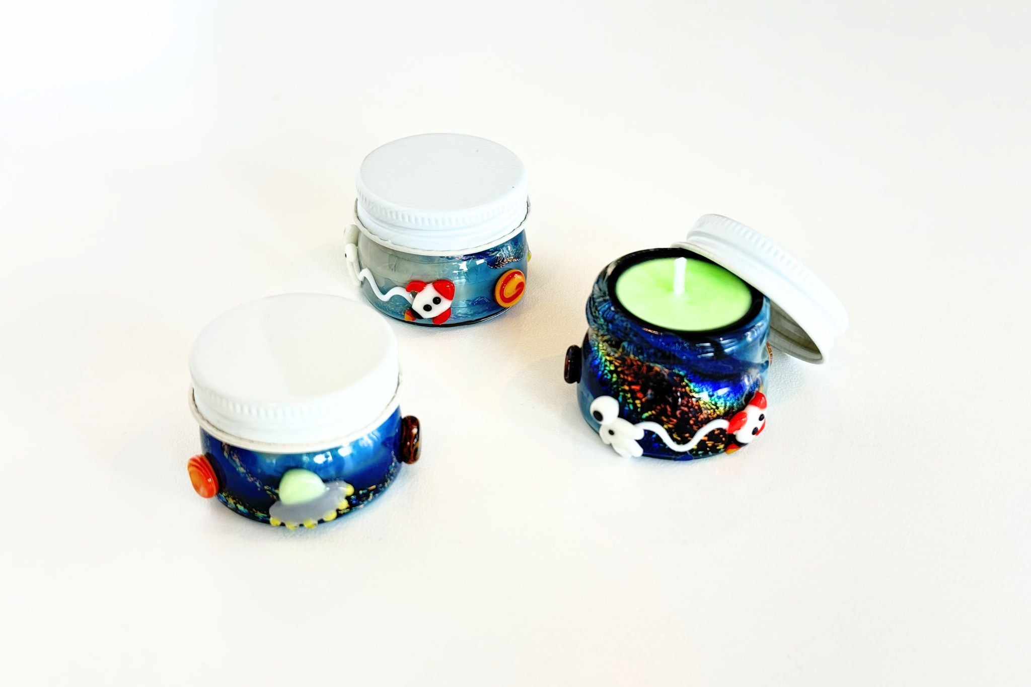 Three small stash jar candles with colorful designs on a white background